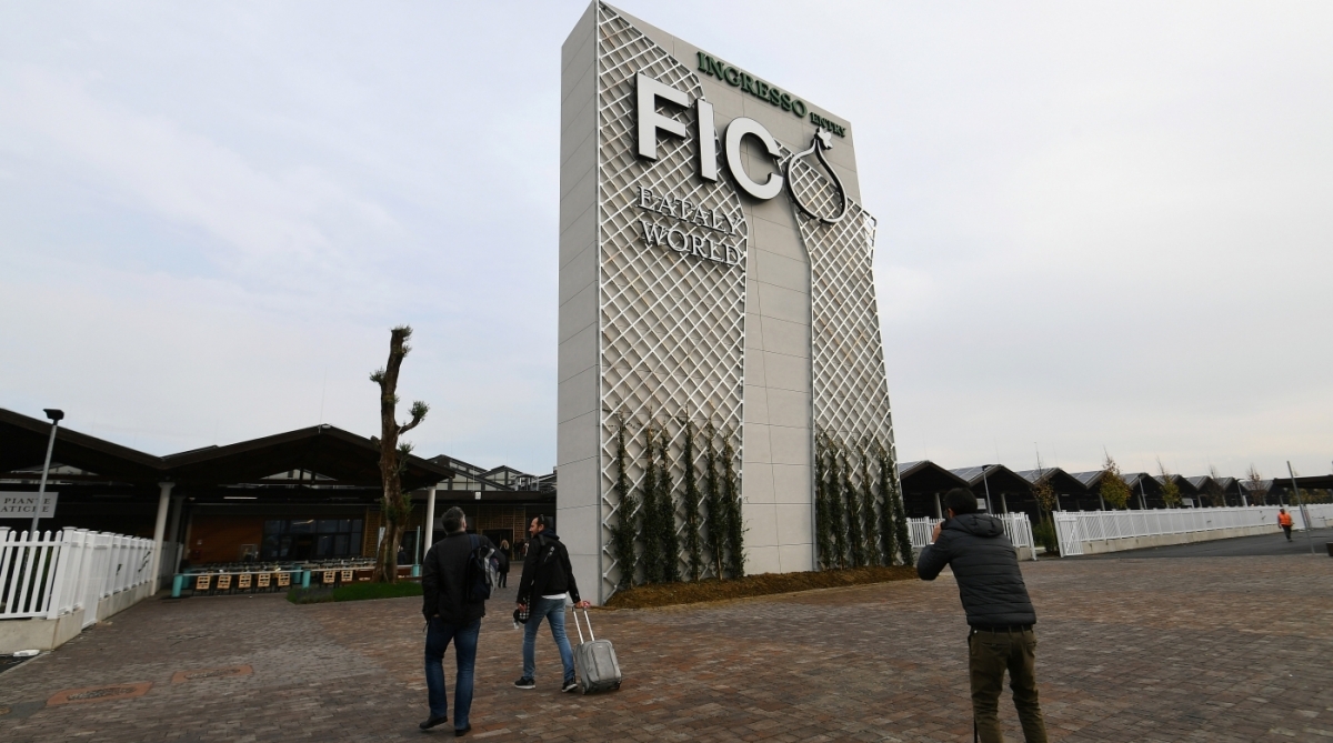 People walk at the entrance to FICO Eataly World agri-food park in Bologna on November 9, 2017. 
FICO Eataly World, said to be the world's biggest agri-food park, will open to the public on November 15, 2017. The free entry park, widely described as the Disney World of Italian food, is ten hectares big and will enshrine all the Italian food biodiversity.  / AFP PHOTO / Vincenzo PINTO
      Caption
