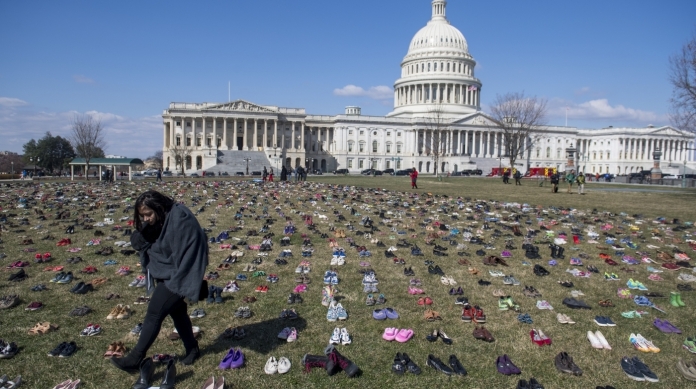 A woman walks through a display of 7,000 pairs of empty shoes to memorialize the 7,000 children killed by gun violence since the Sandy Hook school shooting, organized by the global advocacy group Avaaz, outside the US Capitol in Washington, DC, March 13, 2018. / AFP PHOTO / SAUL LOEB
      Caption
