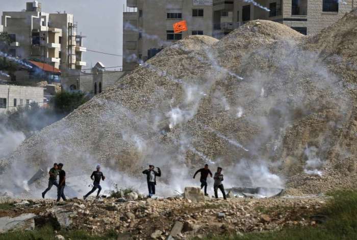 Manifestantes palestinos correm para se proteger do lançamento de gás lacrimogêneo perto do assentamento israelense de Beit El, na Cisjordânia.