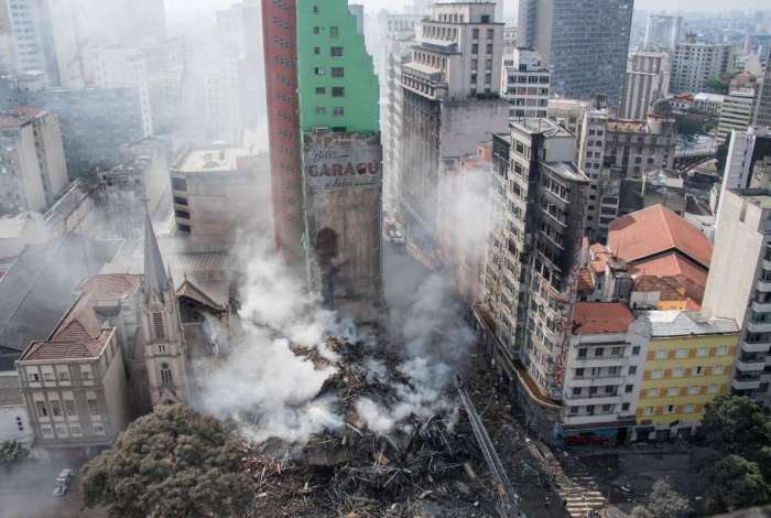 Bombeiros trabalham para resfriar os escombros do prédio incendiado e continuam as buscas no local