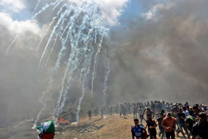 Palestinos fogem de gás lacrimogêneo disparado por forças israelenses perto da fronteira entre a faixa de Gaza e Israel, em 14 de maio