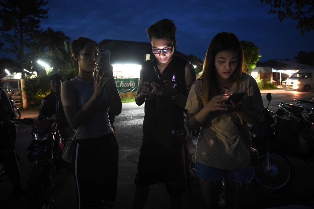 Polícia e militares usam guarda-chuvas para cobrir uma maca perto de um helicóptero e uma ambulância em um aeroporto militar em Chiang Rai (AFP photo / Lillian Suwanrumpha)