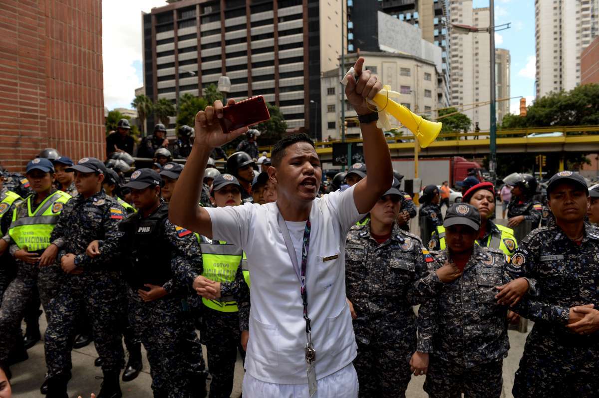 A health worker shouts slogans demanding fair and higher wages during a protest for the lack of medicines, medical supplies and poor conditions in hospitals, in front of a line of police outside the "Dr. JM de los Rios" Children's Hospital in Caracas on August 16, 2018.
Health workers marched Thursday to the government palace marking a month and a half of demonstrations. / AFP PHOTO / Federico PARRA