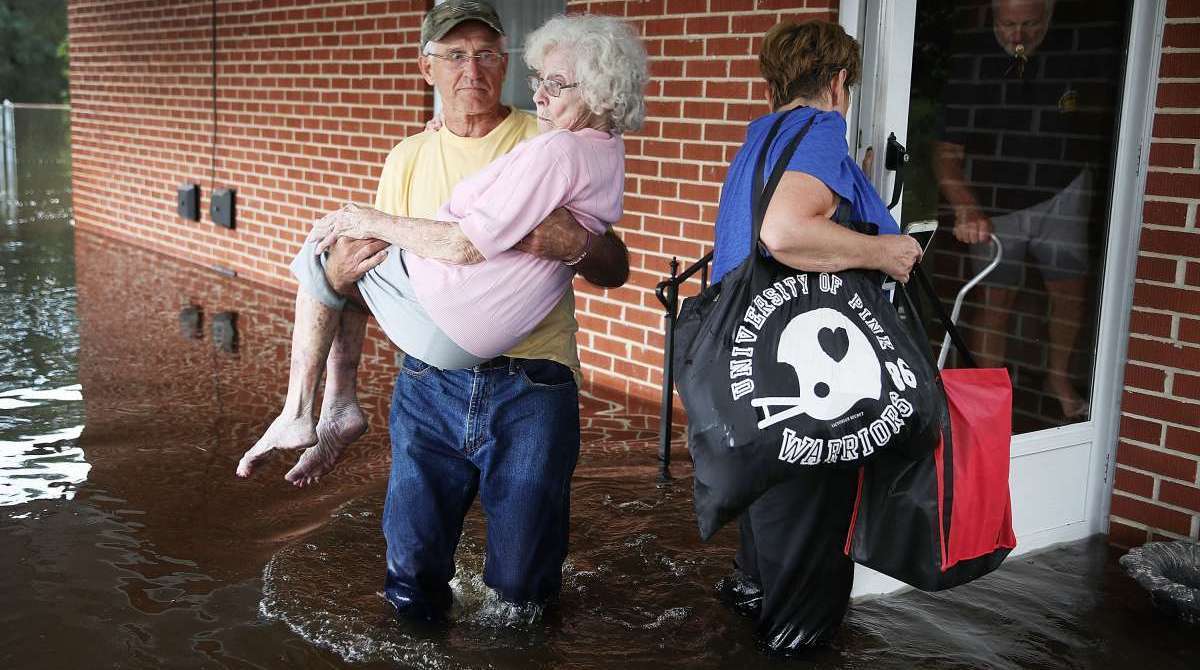 SPRING LAKE, NC - SEPTEMBER 17: Bob Richling carries Iris Darden as water from the Little River starts to seep into her home on September 17, 2018 in Spring Lake, North Carolina. Pam Darden and Iris Darden's son, David Darden jr., help save items from the home as flood waters from the cresting rivers inundate the area after the passing of Hurricane Florence.   
      Caption