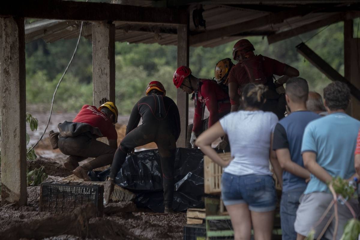 Sob o olhar de moradores, equipes resgatam mais um corpo em meio aos escombros de uma casa - AFP