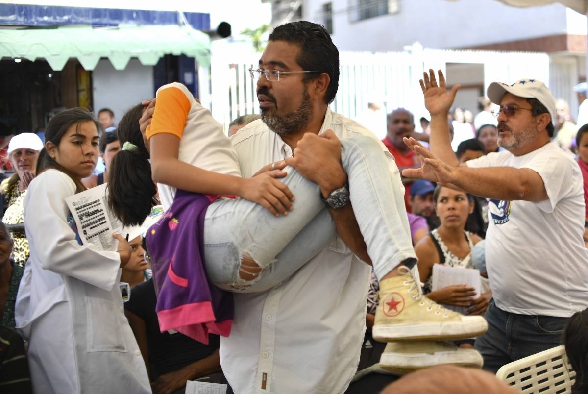 Um voluntário do movimento 'Coalizão Ajuda e Liberdade' carrega uma menina desmaiada durante um campo de atenção médica em Caracas - Yuri Cortez/ AFP