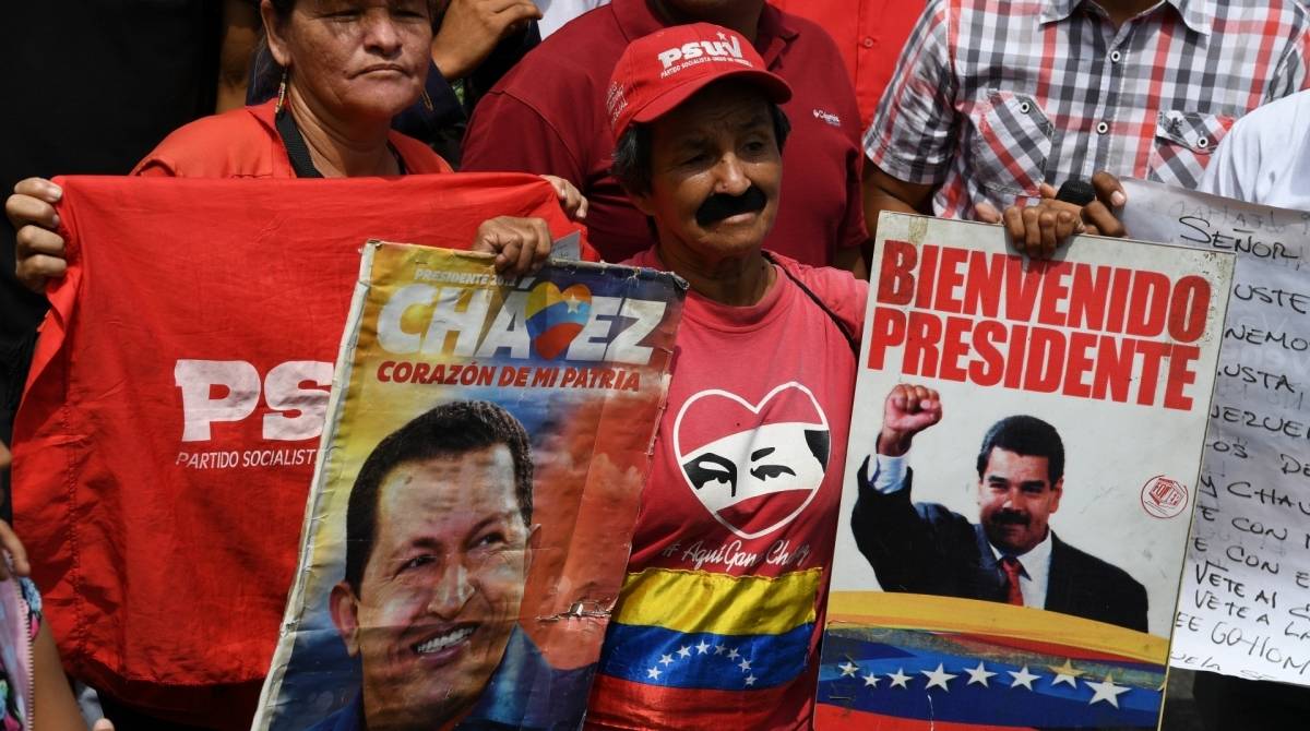 Um apoiador do presidente venezuelano, Nicolas Maduro, exibe cartazes com fotos de Maduro e do falecido líder Hugo Chávez durante um comício no dia 1º de maio 