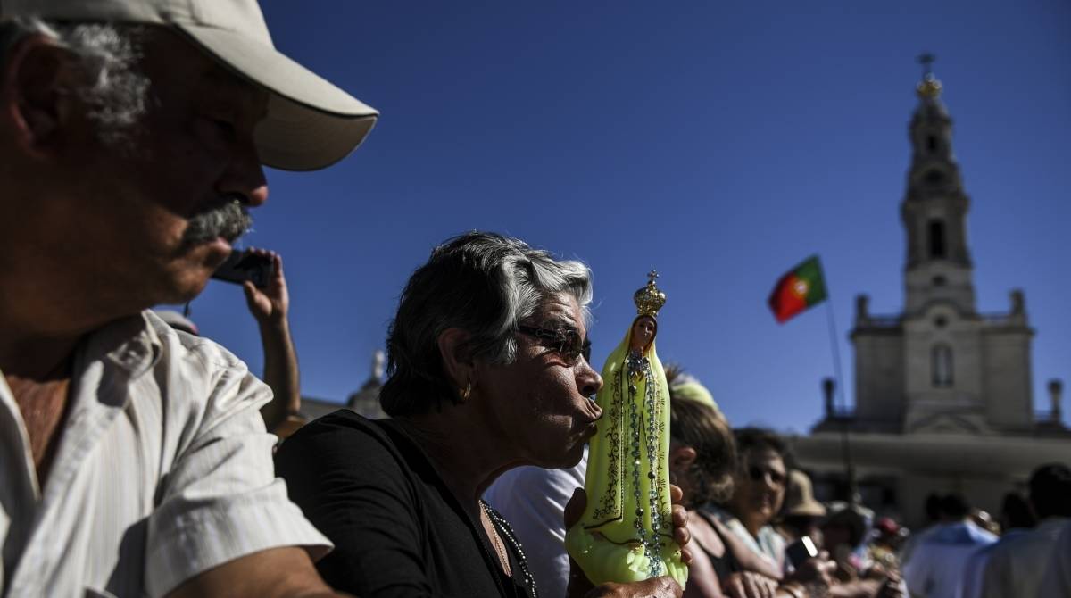 Mulher beija uma figura de Nossa Senhora Fátima durante a procissão no santuário de Fátima, em Fátima, no centro de Portugal, em 13 de maio de 2019