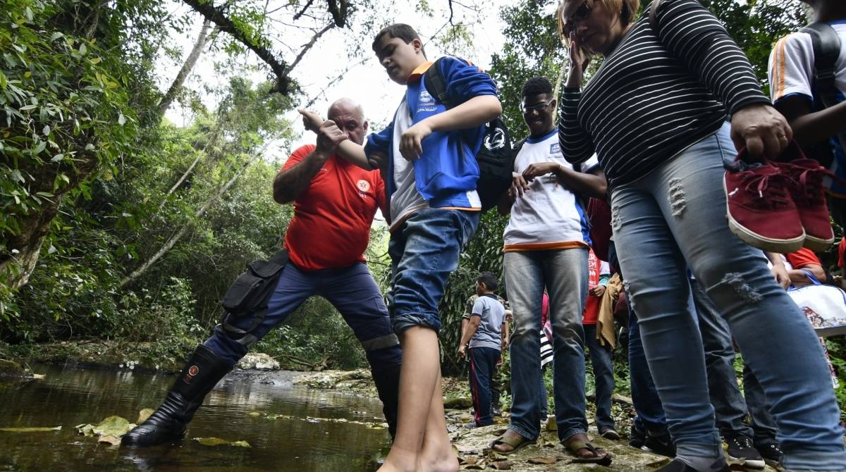 Um guarda ambiental municipal auxilia estudante com deficiÃªncia a tocar a Ã¡gua com os pÃ©s  