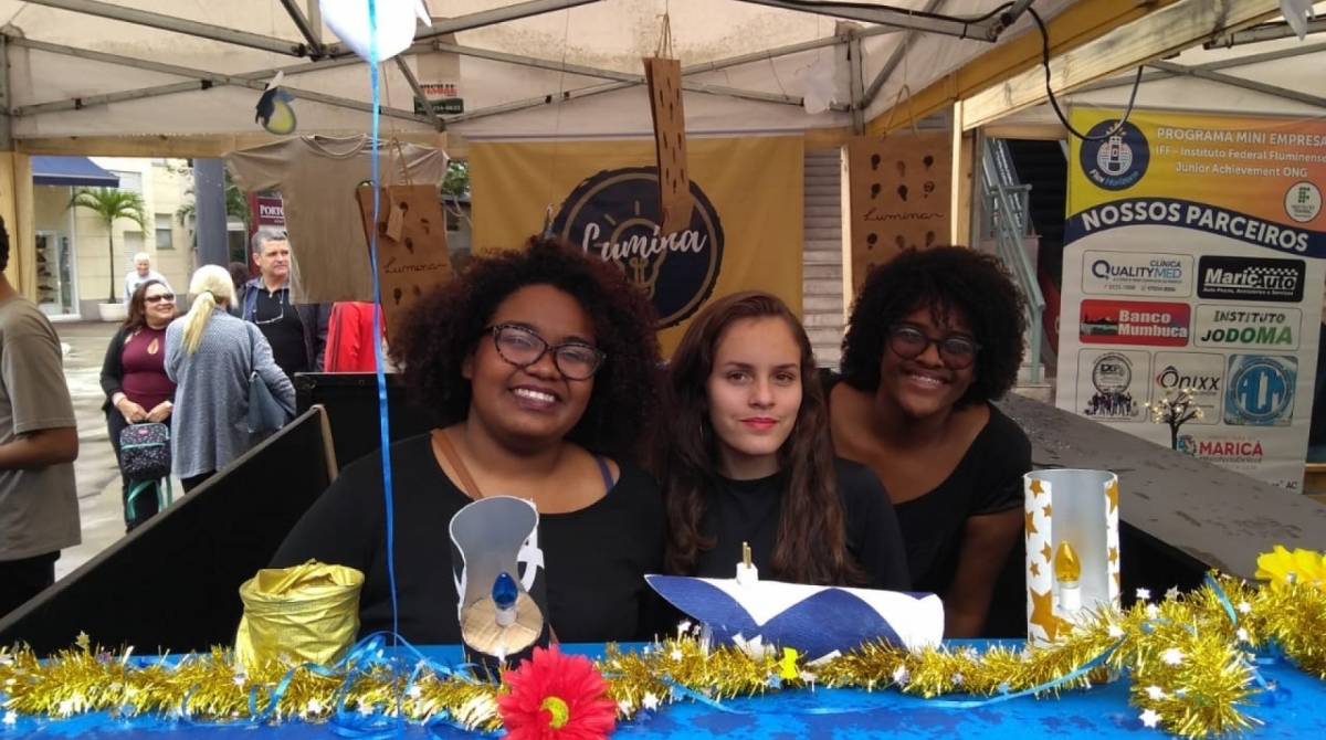 As alunas  mostram algumas luminárias de parede criadas utilizando canos de PVC, papelão, tecido e componentes elétricos