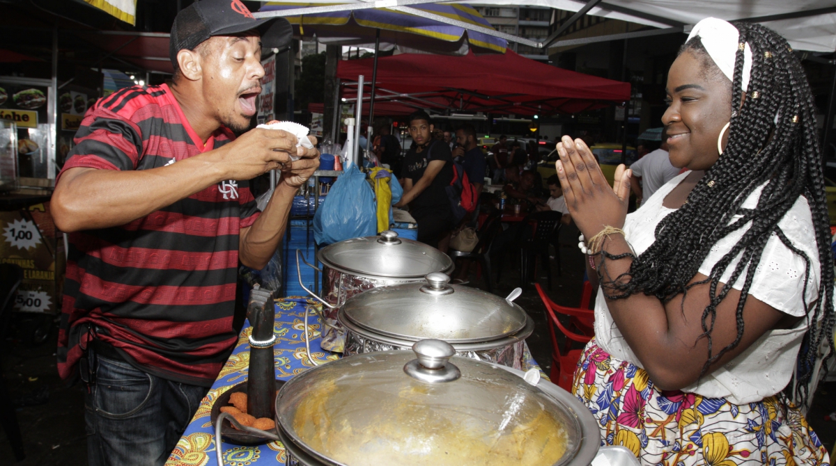 A vendedora Michelle Carvalho (D) oferece o seu acarajé para o flamenguista Gelson dos Santos