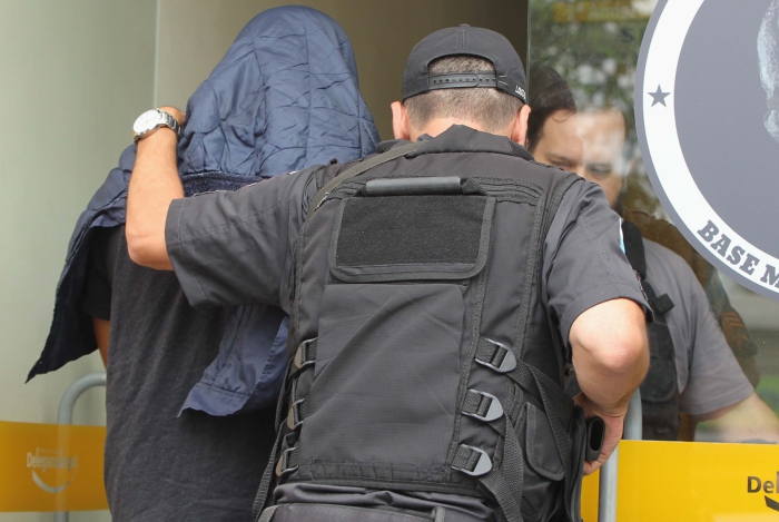 Um dos policiais presos na ação chega à DHBF com a cabeça coberta
