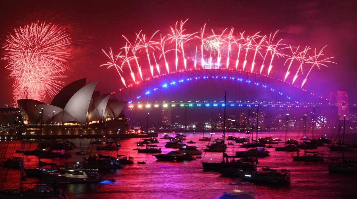New Year's Eve fireworks erupt over Sydney's iconic Harbour Bridge and Opera House (L) during the fireworks show on January 1, 2020. (Photo by PETER PARKS / AFP)
      Caption