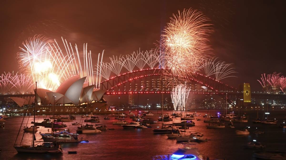 New Year's Eve fireworks erupt over Sydney's iconic Harbour Bridge and Opera House (L) during the fireworks show on January 1, 2020. (Photo by PETER PARKS / AFP)
      Caption