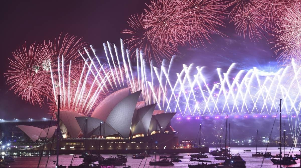 New Year's Eve fireworks erupt over Sydney's iconic Harbour Bridge and Opera House (L) during the fireworks show on January 1, 2020. (Photo by PETER PARKS / AFP)
      Caption