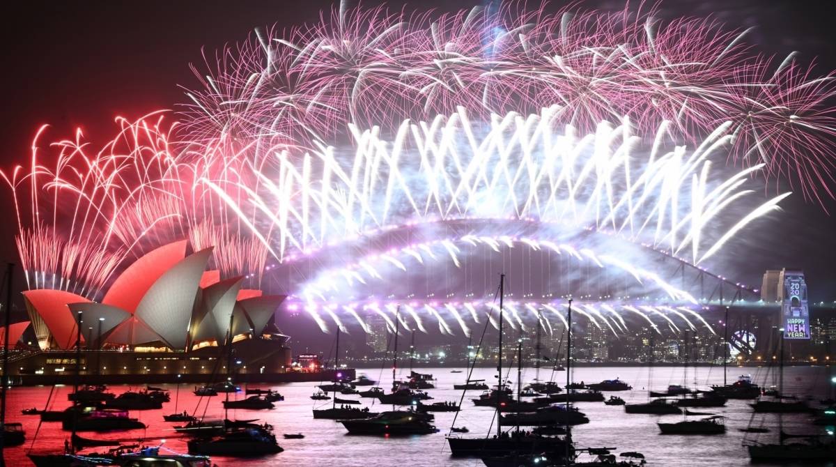 New Year's Eve fireworks erupt over Sydney's iconic Harbour Bridge and Opera House (L) during the fireworks show on January 1, 2020. (Photo by PETER PARKS / AFP)
      Caption