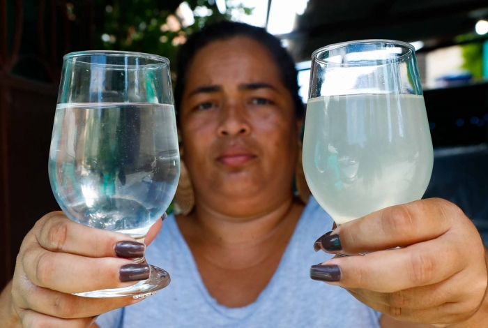 Moradora de Paciência, Jaqueline Leocadio mostra um copo com água limpa e outro com a água turva e suja