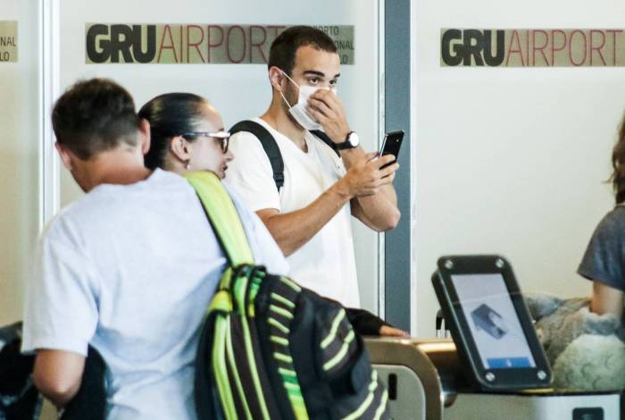Passageiros no Aeroporto Internacional de São Paulo, localizado em Guarulhos, usam máscaras por causa da nova ameaça do coronavírus