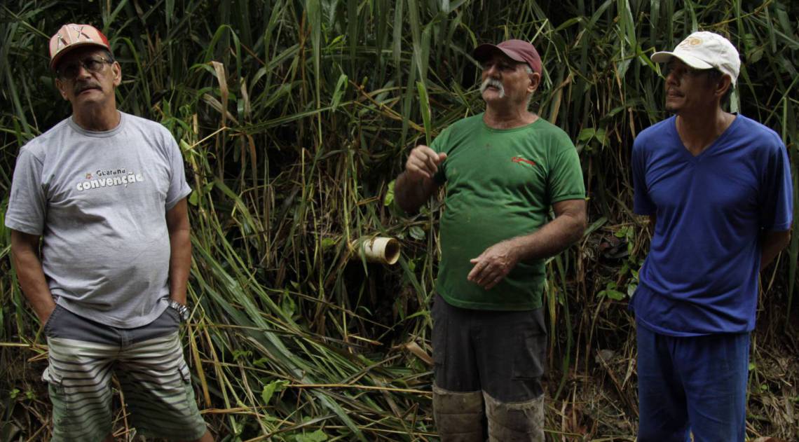 Aílton Antunes (de verde) e Isaías Nascimento sofrem com esgoto despejado diretamente de um cano (detalhe), causando erosão e contaminação em Ponte Coberta, em Paracambi