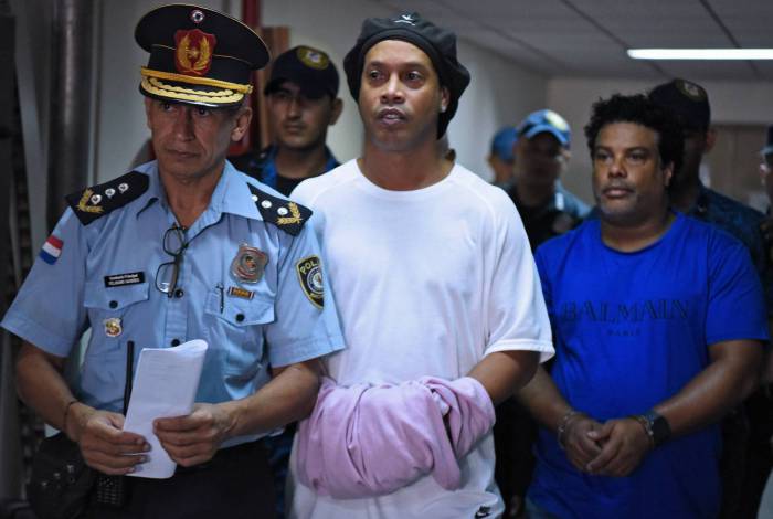 Brazilian retired football player Ronaldinho (C) and his brother Roberto Assis (R) arrive at Asuncion's Justice Palace to appear before a public prosecutor who will decide whether to grant them bail or not following their irregular entry to the country, in Asuncion, on March 7, 2020. - Former Brazilian football star Ronaldinho and his brother have been detained in Paraguay after allegedly using fake passports to enter the South American country, authorities said Wednesday. (Photo by Norberto DUARTE / AFP)