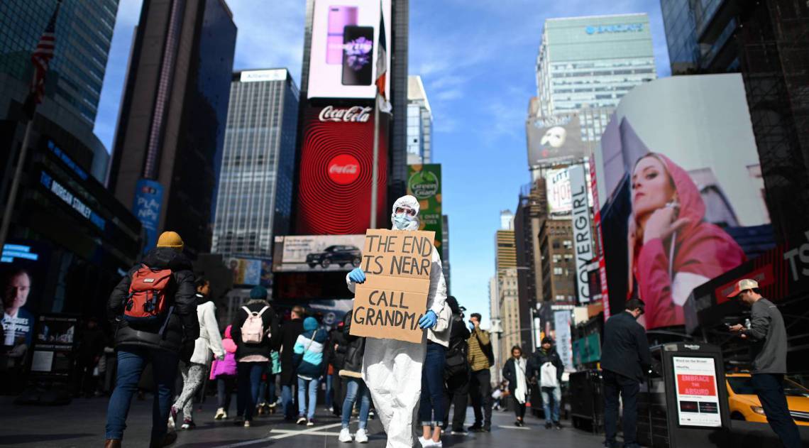 Um homem com roupa de proteção e uma máscara segura uma placa dizendo 'o fim está próximo, ligue para a vovó' na Times Square em 14 de março de 2020 em Nova York - Johannes Eisele/ AFP