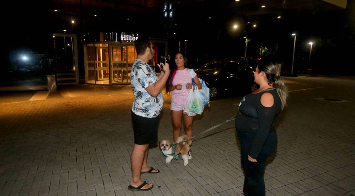 Flay chega ao hotel de máscara e posa com fãs