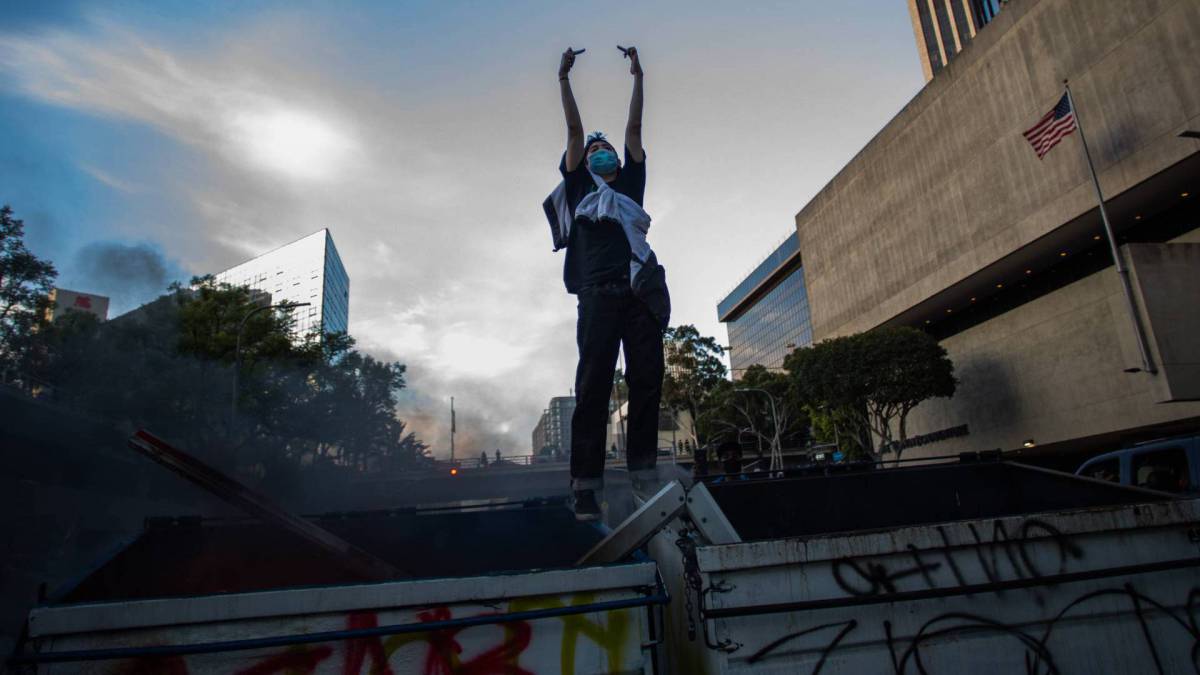 Um homem em cima de latas de lixo em chamas faz gestos contra a polícia no centro de Los Angeles