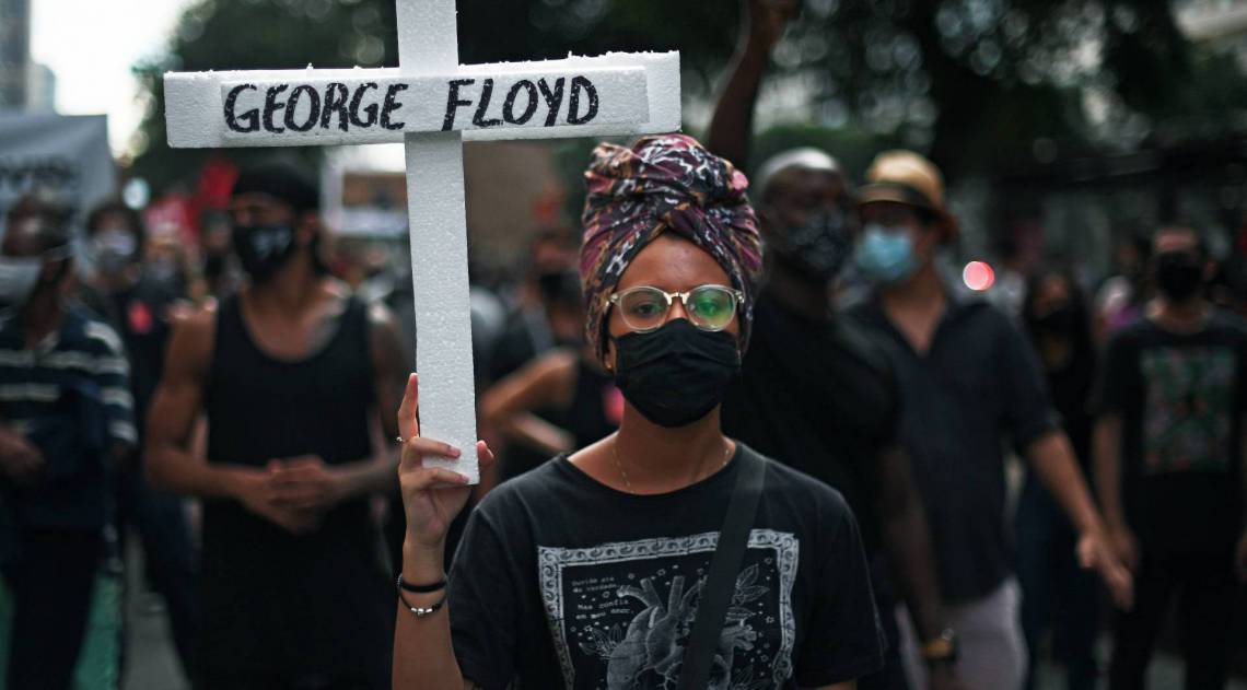 A protester holds a cross with the name of George Floyd, an unarmed black man killed while apprehended by police in Minneapolis, US, during an anti-racism demonstration in which protesters also shouted slogans against Brazilian President Jair Bolsonaro, in Rio de Janeiro, Brazil, on June 7, 2020 amid the COVID-19 novel coronavirus pandemic. - Brazilians took to the streets for rival demonstrations on Sunday for and against Bolsonaro, who has been widely criticized over his response to the coronavirus pandemic. Demonstrators, many dressed in black and wearing face masks, held banners saying: "Everyone for democracy", "Against racism and fascism" and "Terrorism is the government's policy of extermination." (Photo by Carl DE SOUZA / AFP)
      Caption