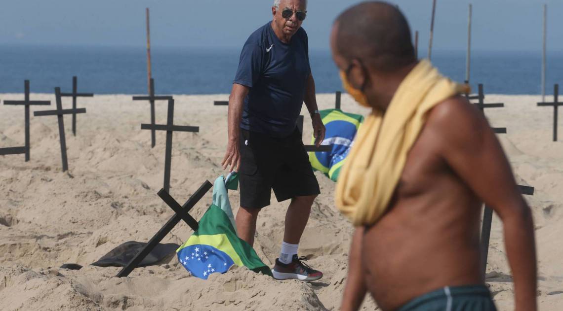 ONG Rio de Paz, faz protesto na praia de Copacabana com 100 covas na areia representando os brasileiros mortos pela covid-19, durante a manifestacao um homem, contrario ao protesto derrubava as cruzes, um ortro homem colocava as cruzes lugar. Na foto,Marcio Antonio do Nascimento,olha pro homem derrubando as cruzes . - Cl&eacute;ber Mendes