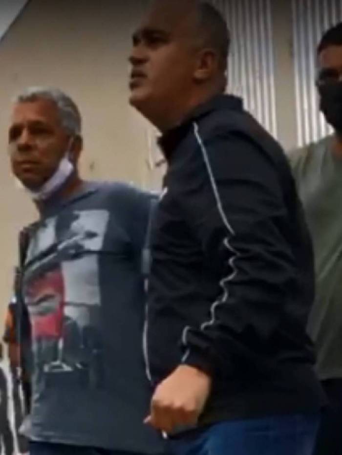 Criminoso de máscara branca sendo levado por policiais 