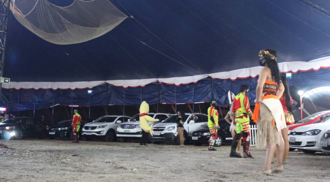 Apresenta&ccedil;&atilde;o do Circo Fant&aacute;stico em Santa Maria, Rio Grande do Sul: carros estacionados de frente para o picadeiro e artistas de m&aacute;scaras