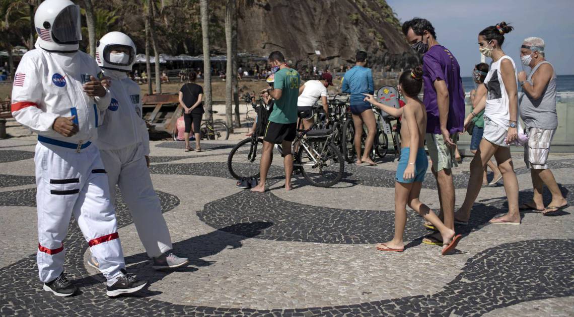 Brazilian accountant Tercio Galdino, 66, and his wife Alicea Galdino walk along Leme beach in protective suits, in Rio de Janeiro, Brazil on July 12, 2020. - Tercio, who has a chronic lung disease, made the protective suits (looking like astronauts gear) at home using suits used by health professionals. He says that, in addition to giving him protection against the new coronavirus, they also wear them for fun, as he has huge interest in astronomy. (Photo by Mauro Pimentel / AFP)
      Caption