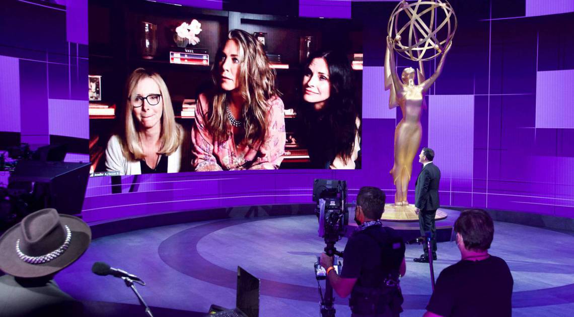 O apresentador Jimmy Kimmel em frente a um telão que mostra a indicada Jennifer Aniston, que estava em casa com as amigas Lisa Kudrow e Courtney Cox, de 'Friends'