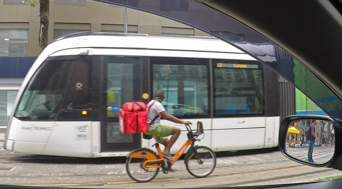 Por fora do carro, o vaiv&eacute;m do VLT e do ciclista reflete o cotidiano do Centro do Rio