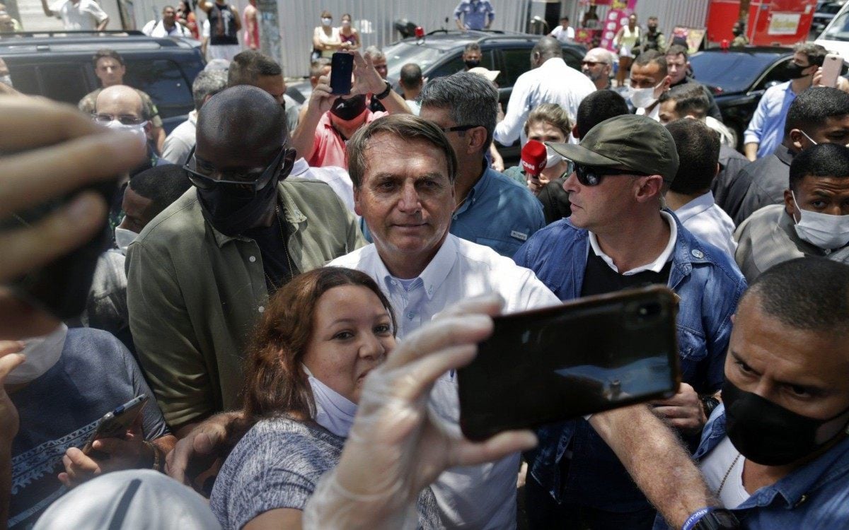 Brazilian President Jair Bolsonaro (C) poses for a selfie with a supporter after voting during the second round of municipal elections at the Rosa da Fonseca Municipal School, in the Military Village, Rio de Janeiro, Brazil, on November 29, 2020. - Brazilians go to the polls Sunday to chose mayors in 57 cities, including Sao Paulo and Rio de Janeiro, the most rich and populated, in a runoff marked by the economic crisis and an upsurge of the new coronavirus. (Photo by Andre Coelho / AFP)
      Caption - AFP