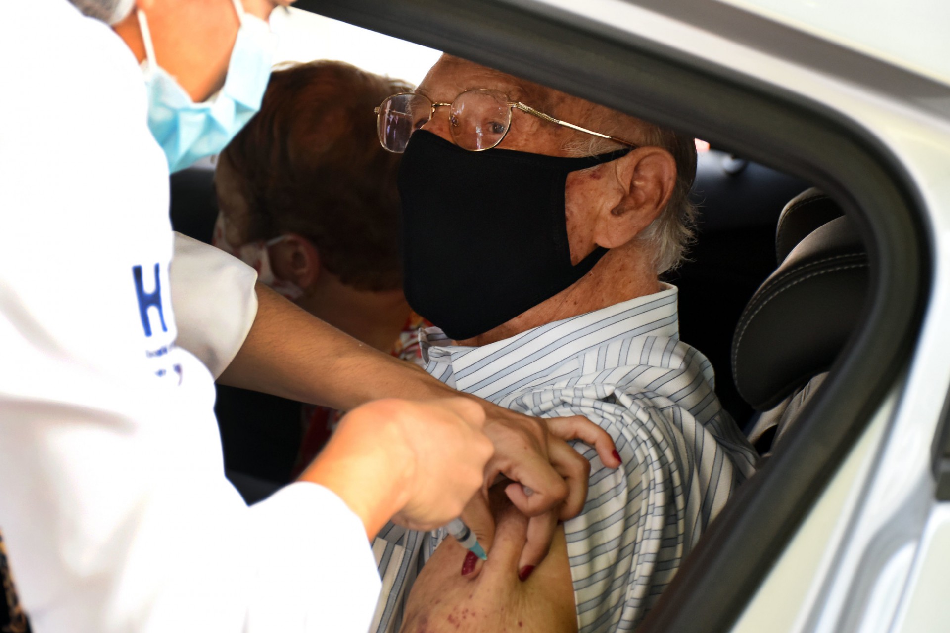 Idoso sendo imunizado dentro do carro, em estande de vacina&ccedil;&atilde;o, na Uerj - Carlos Magno