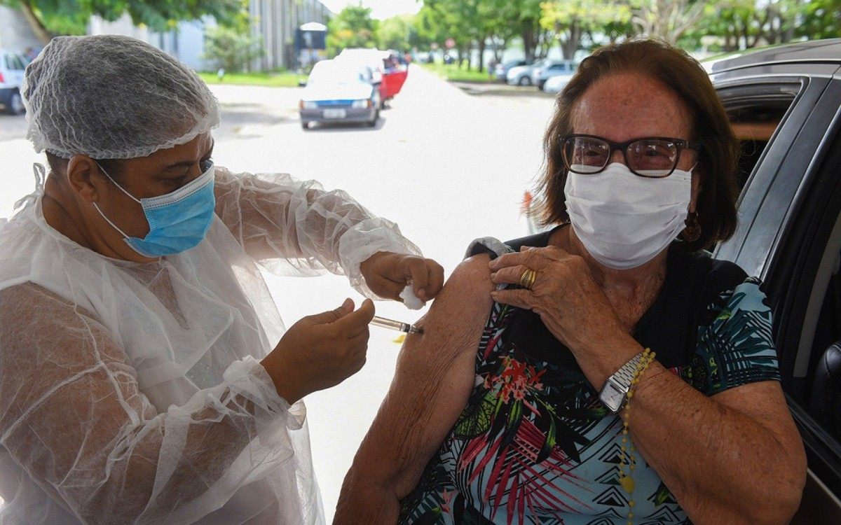 A professora Maria da Penha Fernandes, de 99 anos, recebe a primeira dose da vacina contra a Covid-19.