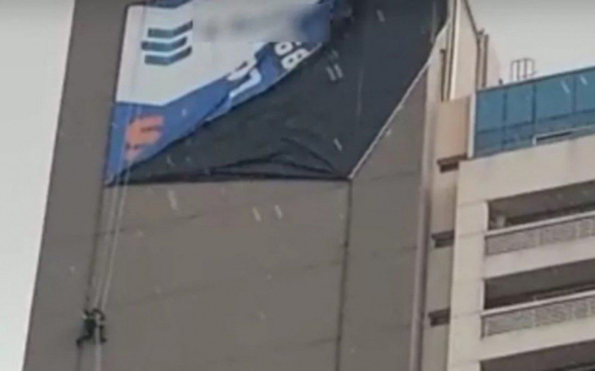 Homem fica pendurado em fachada de prédio ao instalar lona em meio ao temporal - Reprodução/TV Anhanguera