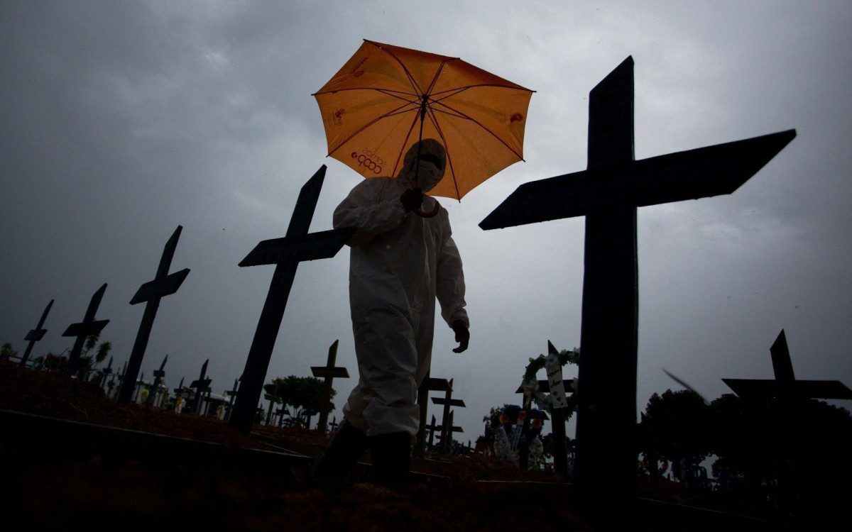 A worker wearing a protective suit and carrying an umbrella walks past the graves of COVID-19 victims at the Nossa Senhora Aparecida cemetery, in Manaus, Brazil, on February 25, 2021. - Brazil surpassed 250,000 deaths due to COVID-19. (Photo by MICHAEL DANTAS / AFP)
      Caption - AFP