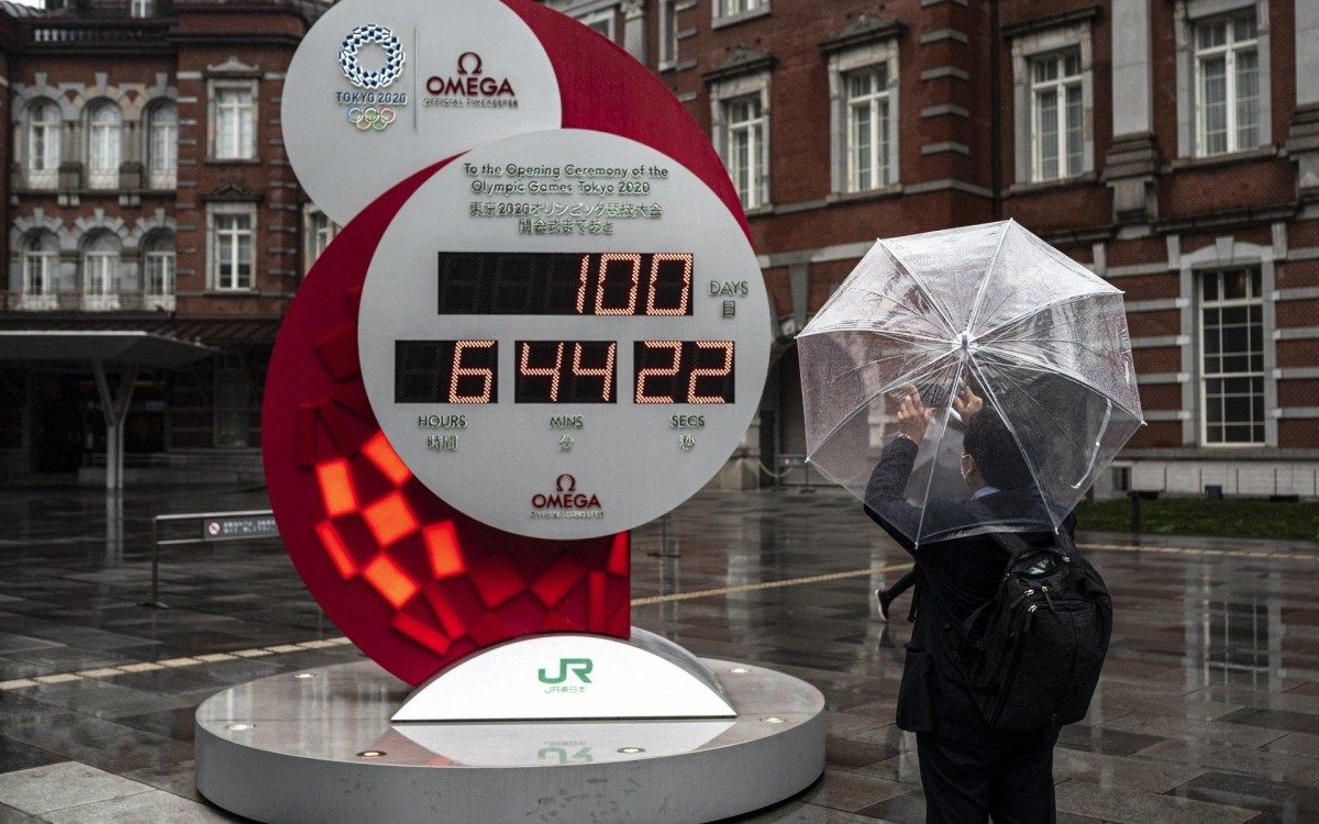 A man takes a picture of a countdown clock for the Tokyo 2020 Olympic and Paralympic Games 100 days before the opening ceremony, outside a Tokyo station in Tokyo on April 14, 2021. (Photo by Charly TRIBALLEAU / AFP) - Charly TRIBALLEAU / AFP