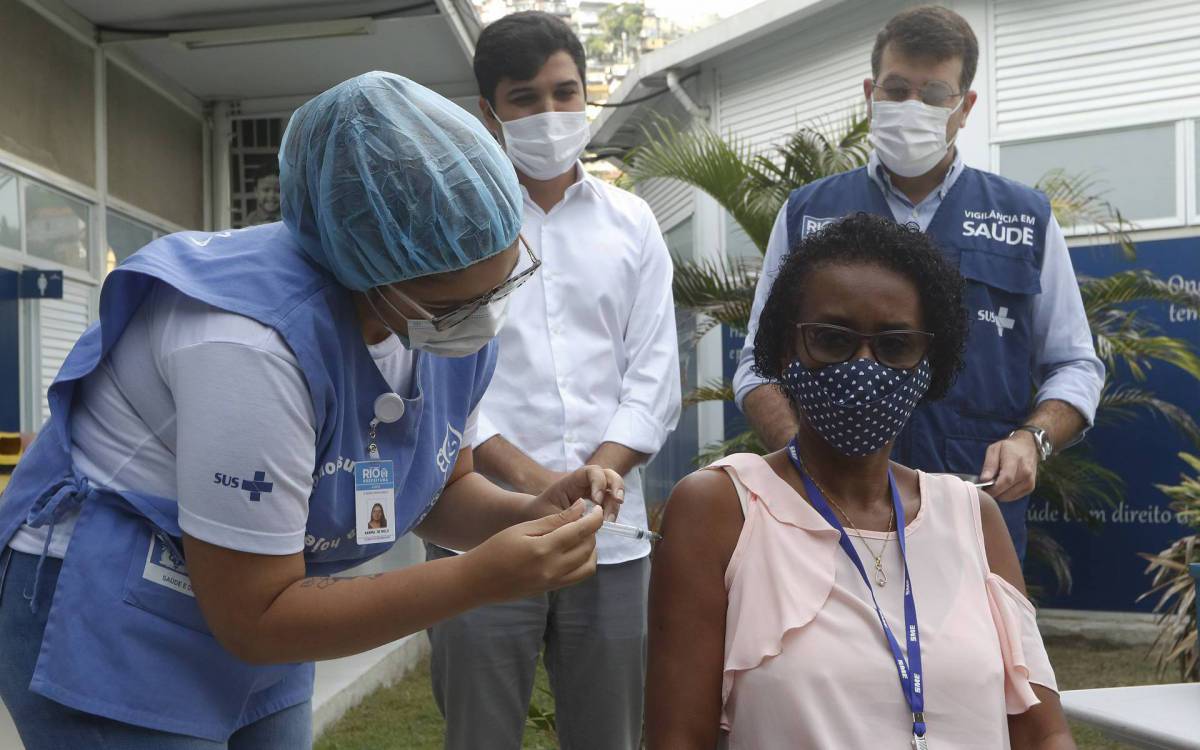 Geral - Inicio da Vacina&ccedil;ao de profissionais da educa&ccedil;ao da rede publica. Profissinais da educa&ccedil;ao basica come&ccedil;am a ser vacinados contra a Covid-19, na Clinica da Familia Sergio Vieira Mello, no Catumbi, regiao central do Rio. Na foto, secretarios de saude e educa&ccedil;ao, Daniel Soranz, de colete azul e Renan Ferreirinha, de blusa branca, com Eliete Matos, agente de educa&ccedil;ao infantil, primeira a ser vacinada.