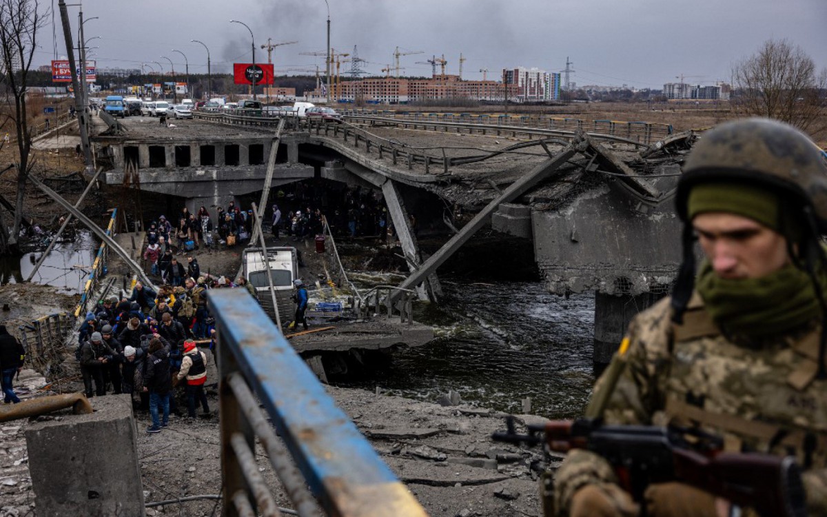 Militar ucraniano observa os evacuados atravessarem uma ponte destruída enquanto fugiam da cidade de Irpin, a noroeste de Kiev