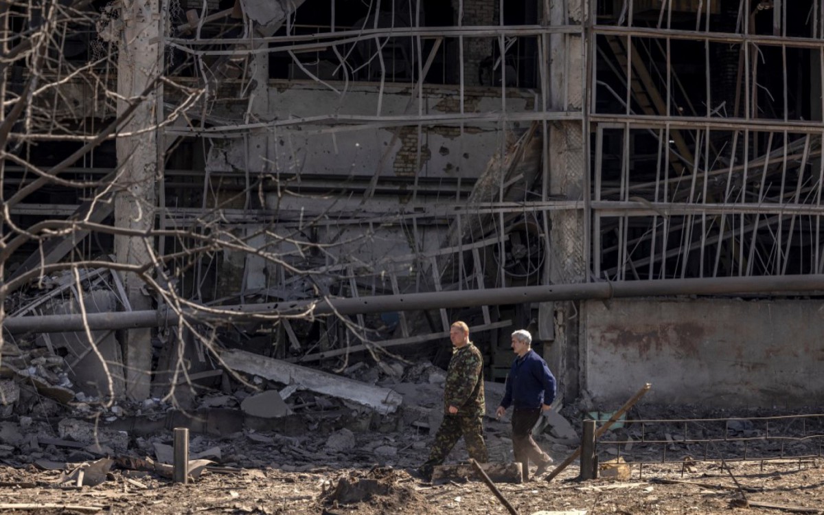 Pessoas passam por um prédio danificado no complexo militar-industrial da empresa Vizar, depois que o local foi atingido por ataques russos durante a noite, na cidade de Vyshneve, subúrbios do sudoeste de Kiev, na Ucrânia - FADEL SENNA / AFP