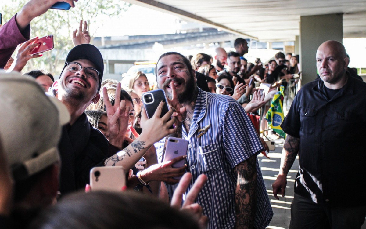 Todo sorridente, Post Malone chega ao Rio e posa com fãs no aeroporto