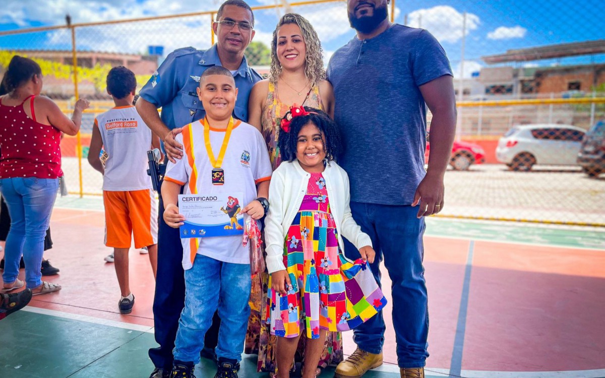 O pai Alexandre Oliveira, a m&atilde;e Sara e a irm&atilde; Ellen orgulhosos, ao lado do sargento Lacerda, na formatura de Enzo &Aacute;vila