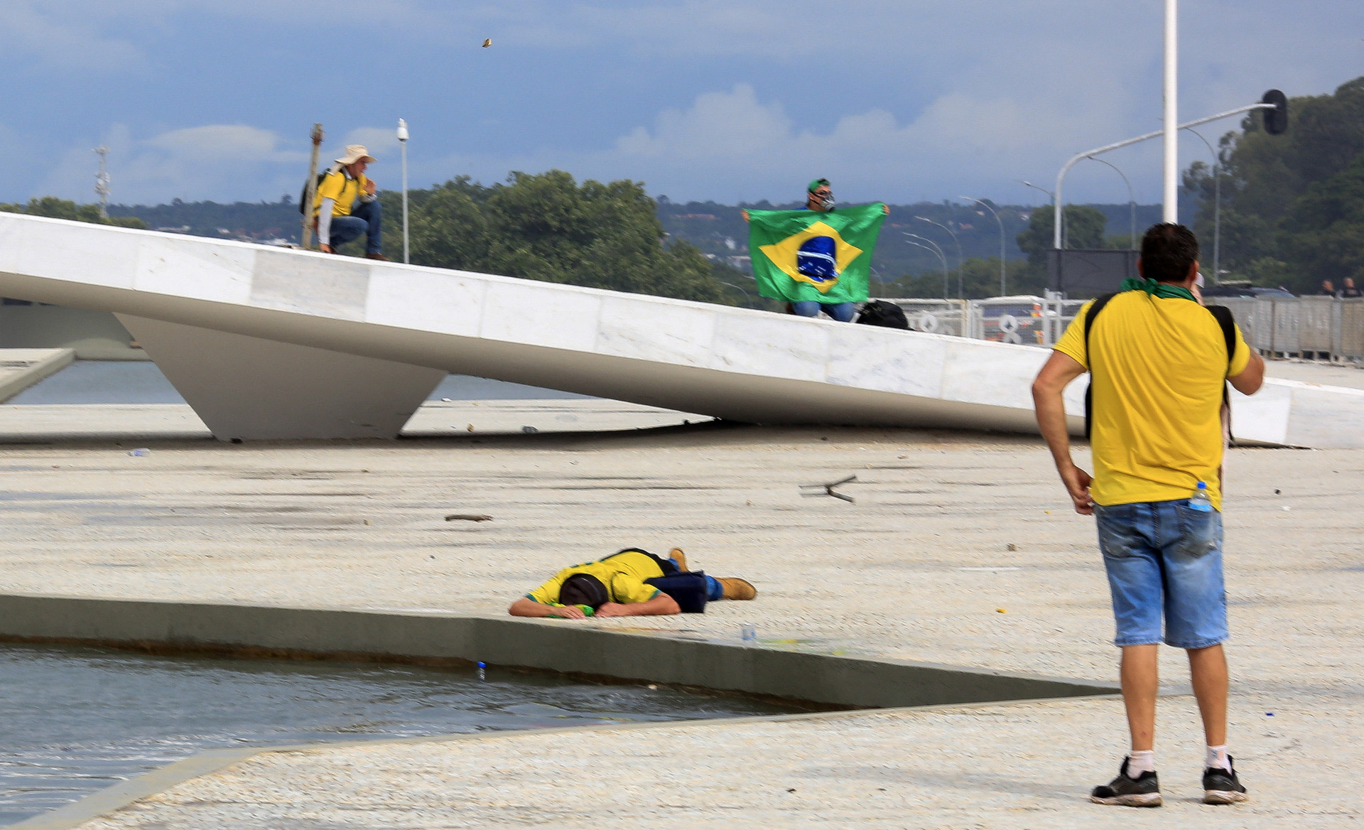 A supporter of Brazilian former President Jair Bolsonaro lies on the ground as others clash with security forces as they invade Planalto Presidential Palace in Brasilia on January 8, 2023. Hundreds of supporters of Brazil's far-right ex-president Jair Bolsonaro broke through police barricades and stormed into Congress, the presidential palace and the Supreme Court Sunday, in a dramatic protest against President Luiz Inacio Lula da Silva's inauguration last week.
 - Sergio Lima / AFP