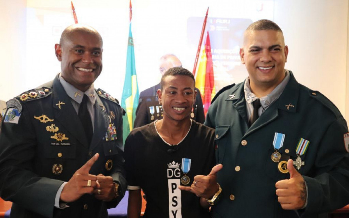 Guto (ao centro) e o Sargento PM Paulo Aguiar (D) com as medalhas M&eacute;rito Embaixador da Paz no Brasil
