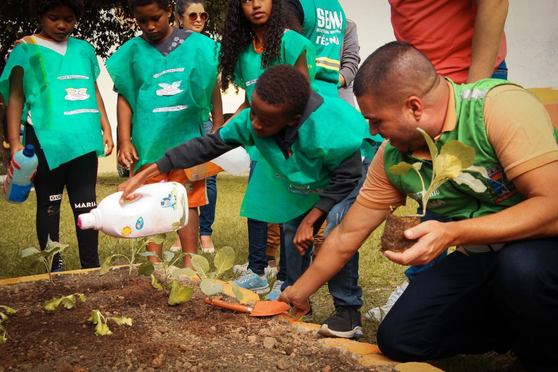 Secret&aacute;rio Igo Menezes observa um aluno regando uma planta no Ciep Constantino Reis - Kristian Amarante / PMBR
