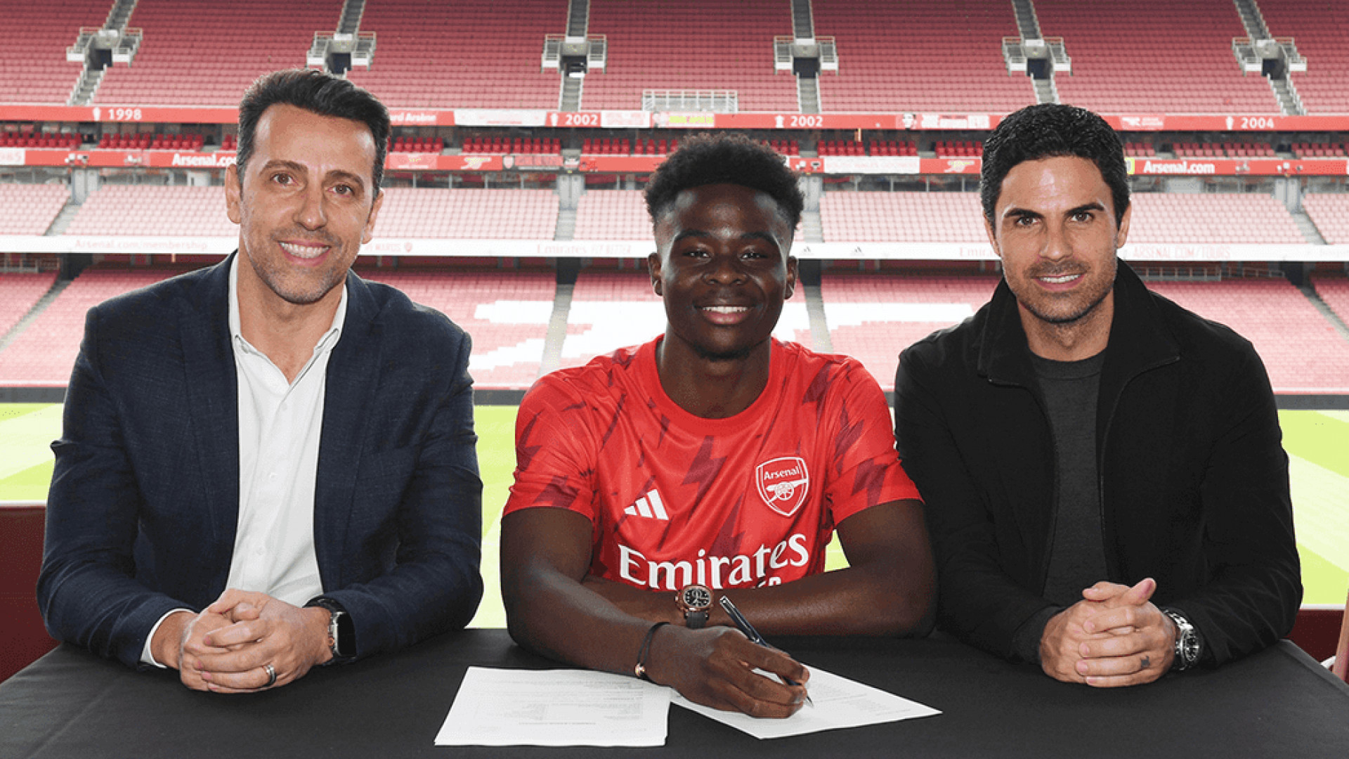 Saka assinando seu novo contrato junto do brasileiro Edu Gaspar de Mikel Arteta   - Divulgação / Arsenal