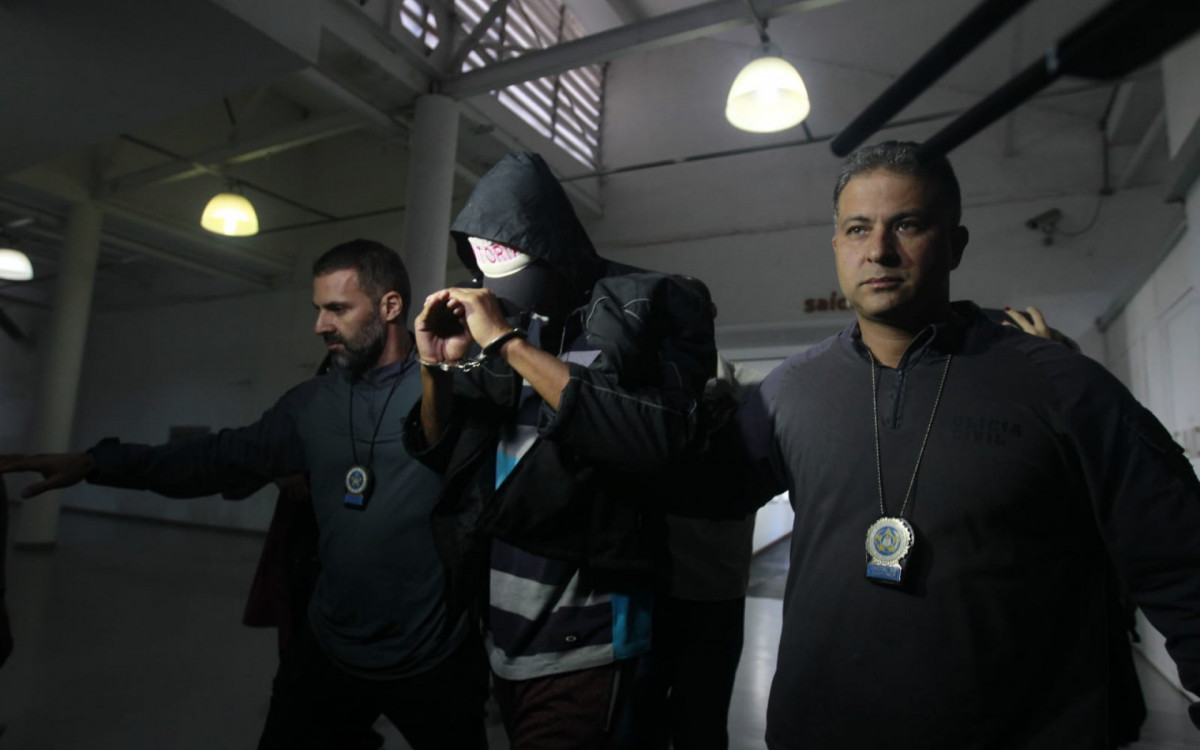 Jeander Vinicius da Silva Braga chegou à Cidade da Polícia algemado e tentando esconder o rosto - Reginaldo Pimenta/Agência O Dia